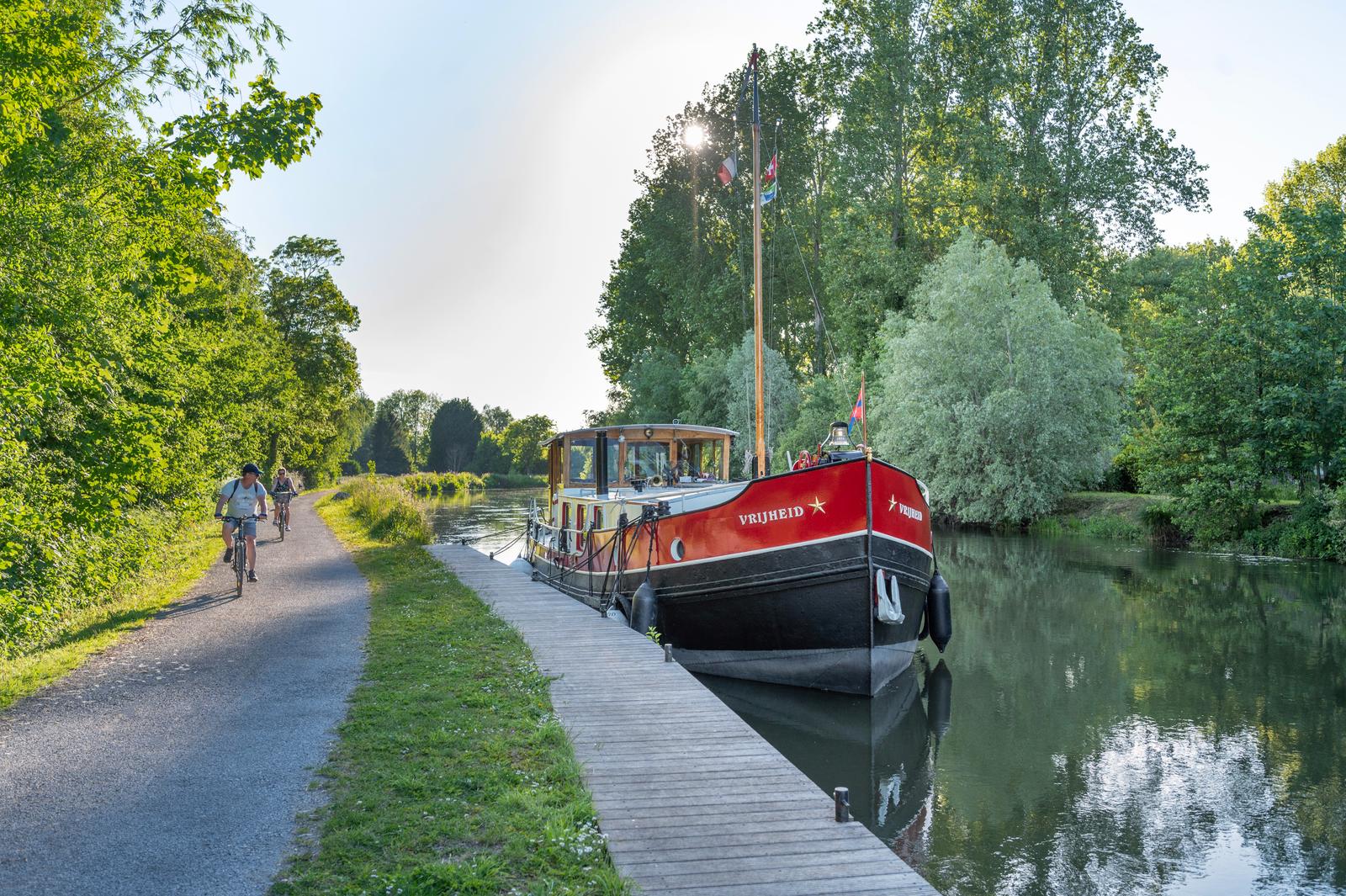 Long : péniche à quai et cyclistes sur le chemin de halage